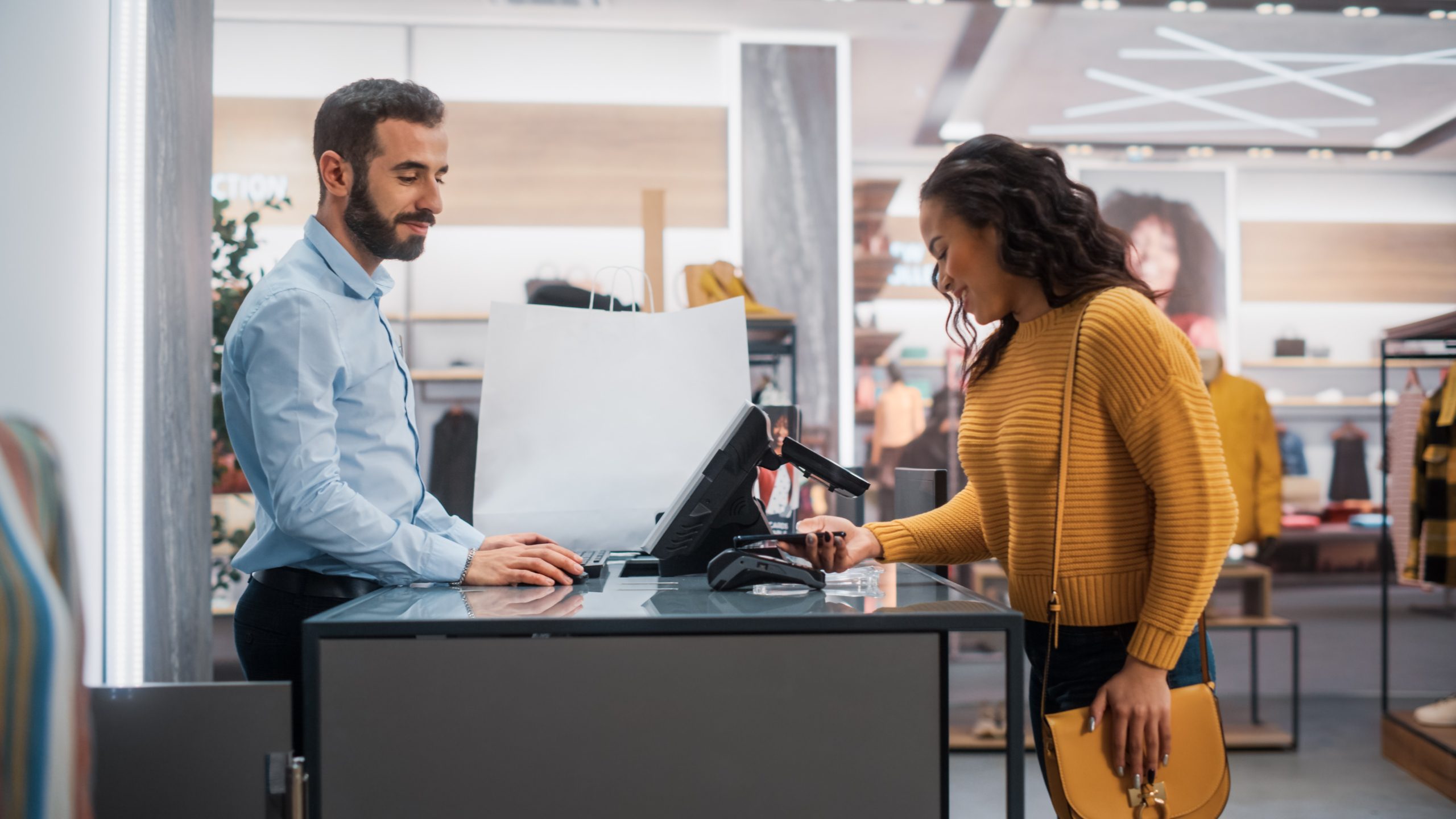 Customer making a contactless payment at a retail checkout counter while a cashier processes the transaction.